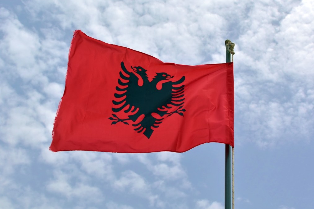 Albania national flag waving in wind on background of blue cloudy sky.